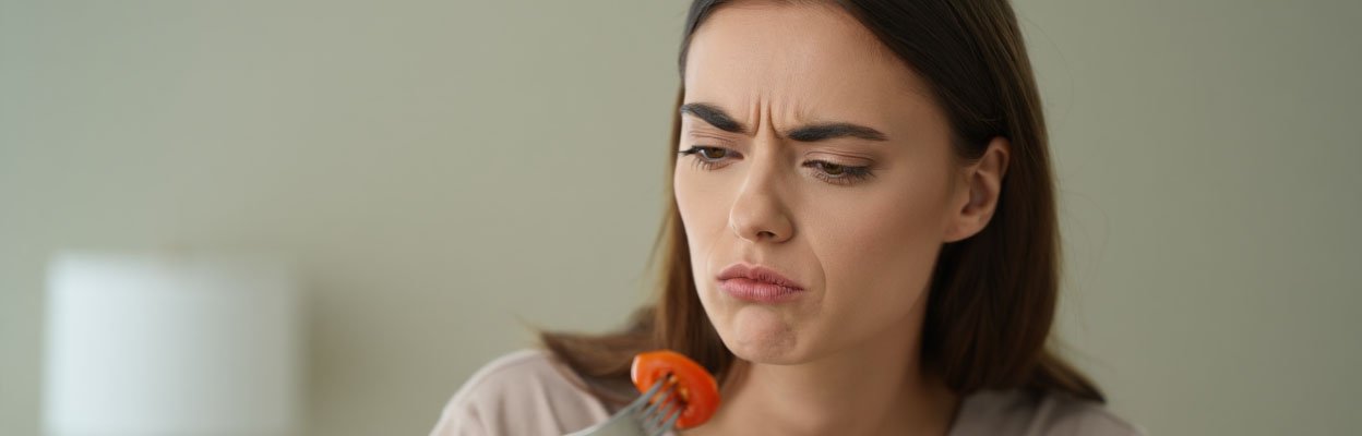 Девушка хмуро смотрит на кусочек помидора